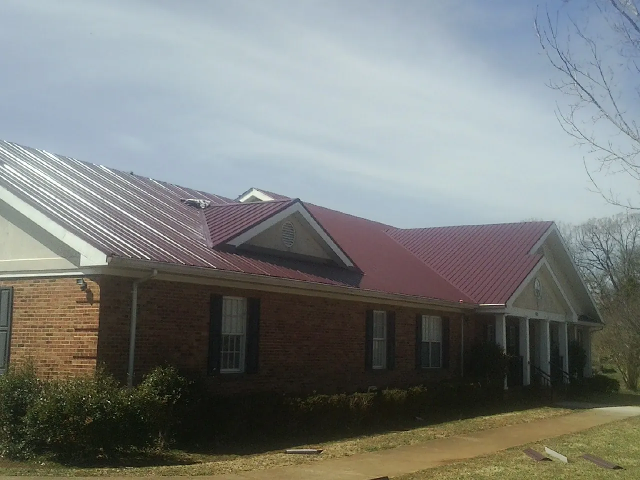 Red metal roof with gabled entries on a long brick building, from a Hail Damage Roof Repair job in Boulevard