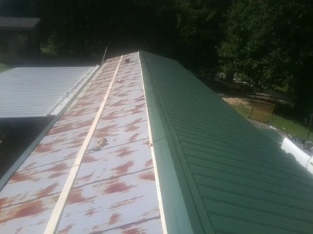 Old rusted panels beside newly installed green metal roofing — Wind Damage Roof Repair by Roofing Brothers in Boulevard