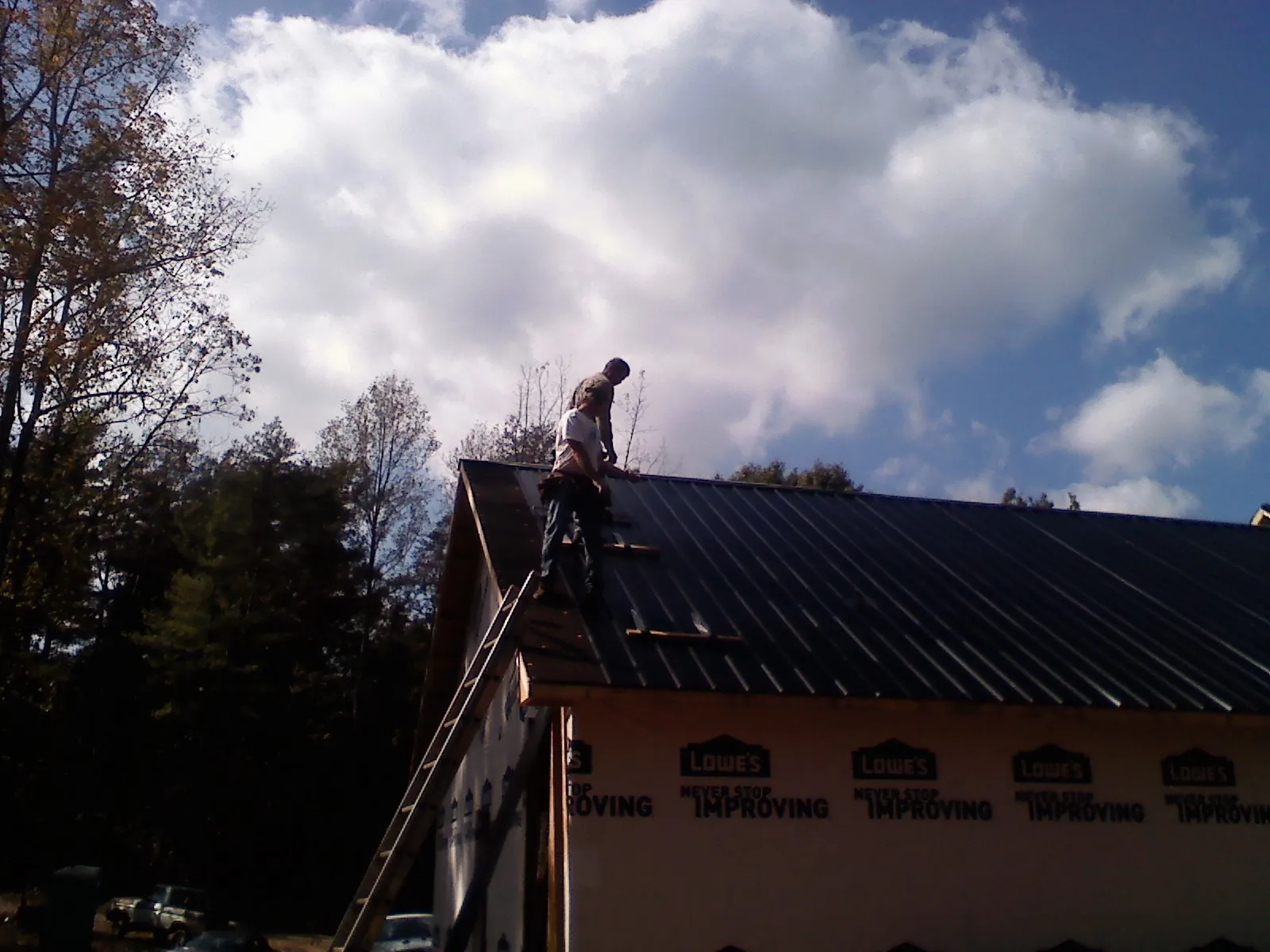 Roofer fastening dark metal panels high against a cloudy sky, from a Roof Inspection job in Boulevard